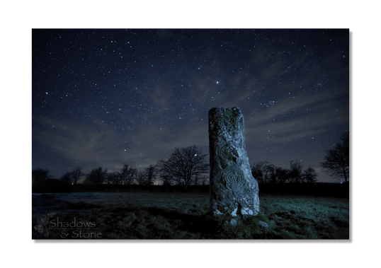 The night sky above the spiral covered solitary remainder of a destroyed passage tomb.